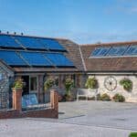 Middle Oaks Facilities Building with Solar Panels Modern stone building with solar panels and skylights, identified as “Middle Oaks.” Bright hanging baskets and flower beds decorate the area, with a paved patio and benches for guests.
