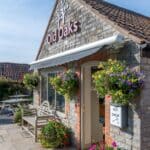 Old Oaks Reception & Shop Charming stone building with flower baskets and signage reading “Old Oaks Reception & Shop.” A key drop box is visible near the entrance under a white awning.